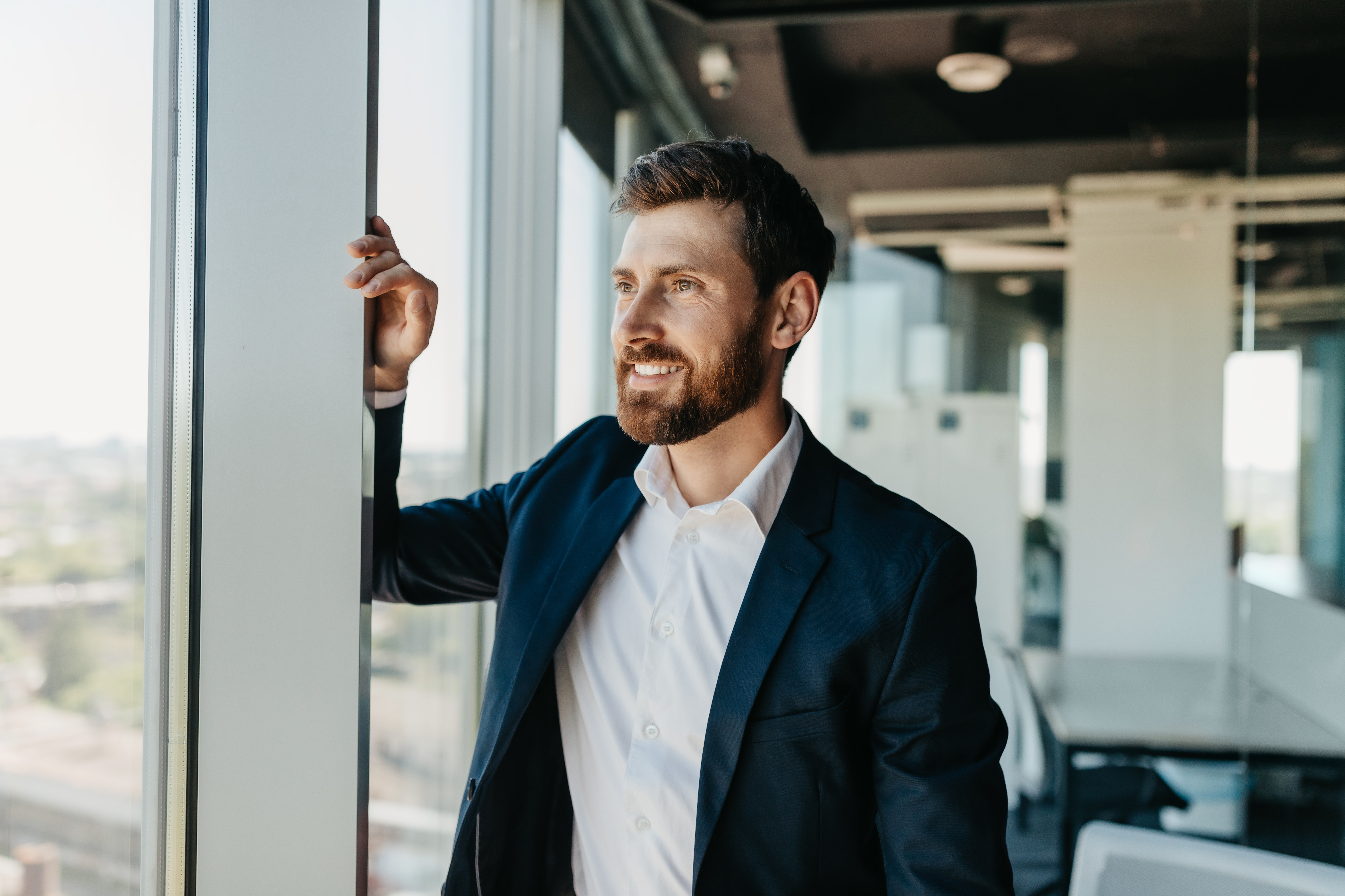 confident-business-man-suit-standing-modern-coworking-office-room-leaning-window-smiling