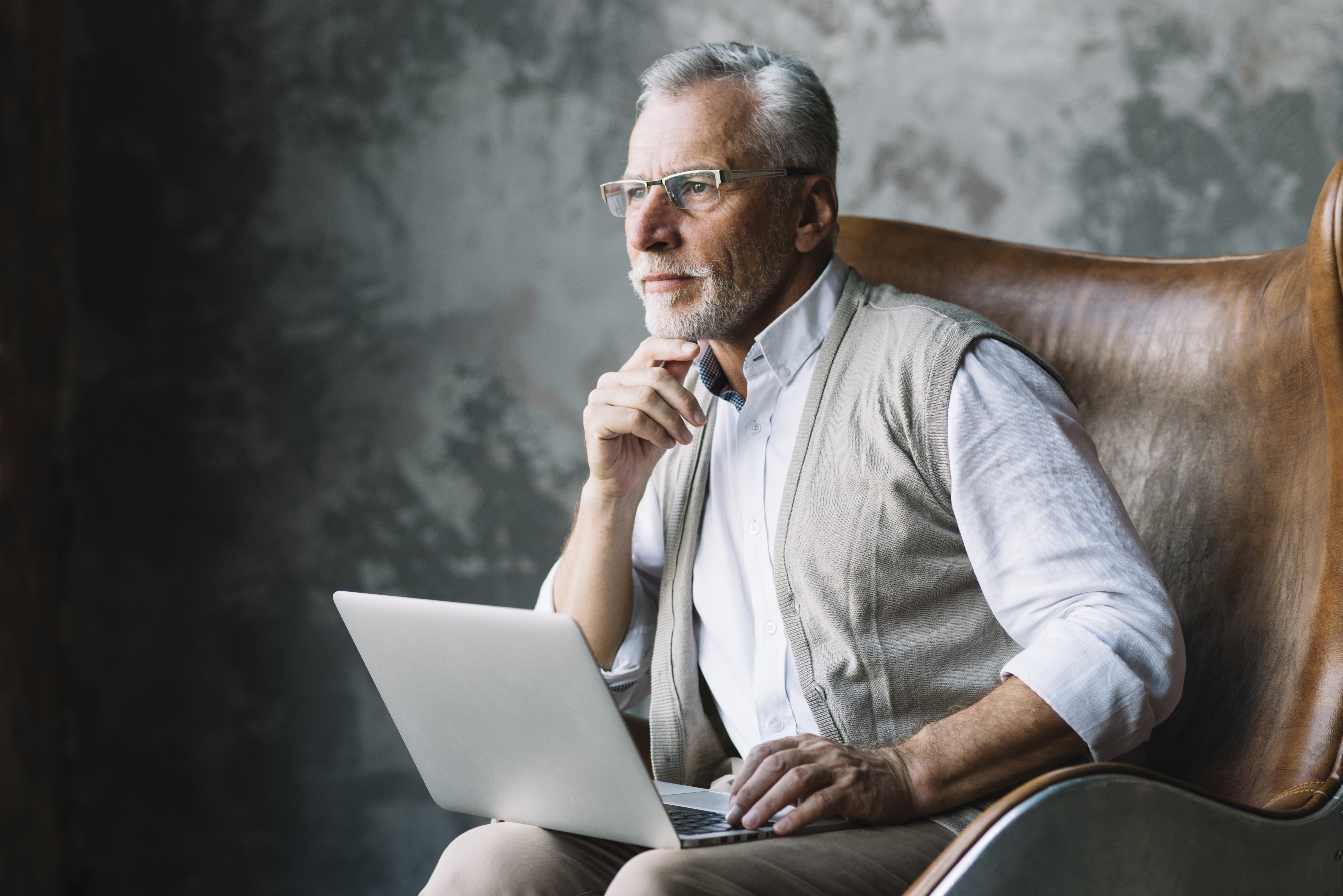 contemplated-elderly-man-sitting-chair-with-laptop-against-grunge-background